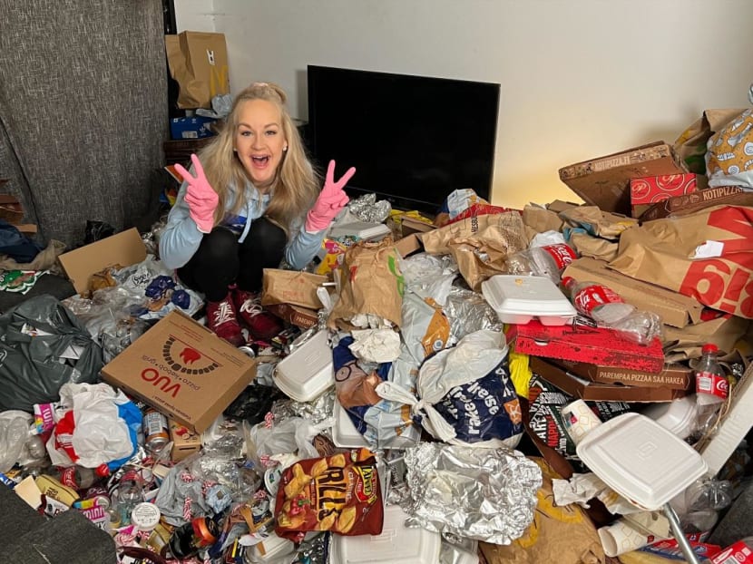 Finnish TikTok "cleanfluencer" Auri Kananen wearing pink gloves and making victory signs as she sits on a pile of trash and food remains in a flat in Helsinki, Finland, on Jan 19, 2023.