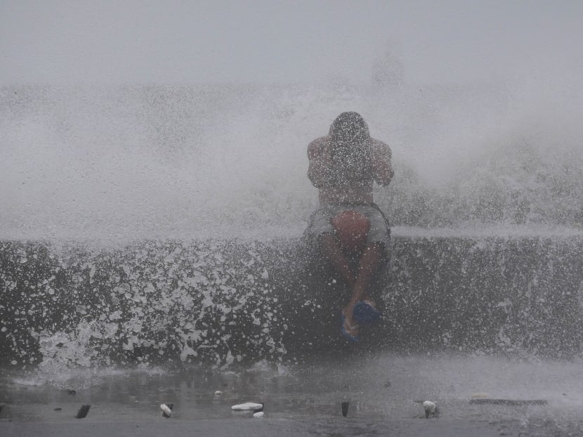 A Filipino reacts as he is hit by waves along a promenade in Manila, Philippines. Photo: AP