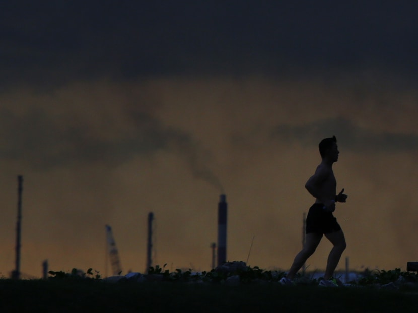 A man runs past a chimney giving off emissions in an industrial area of Singapore.