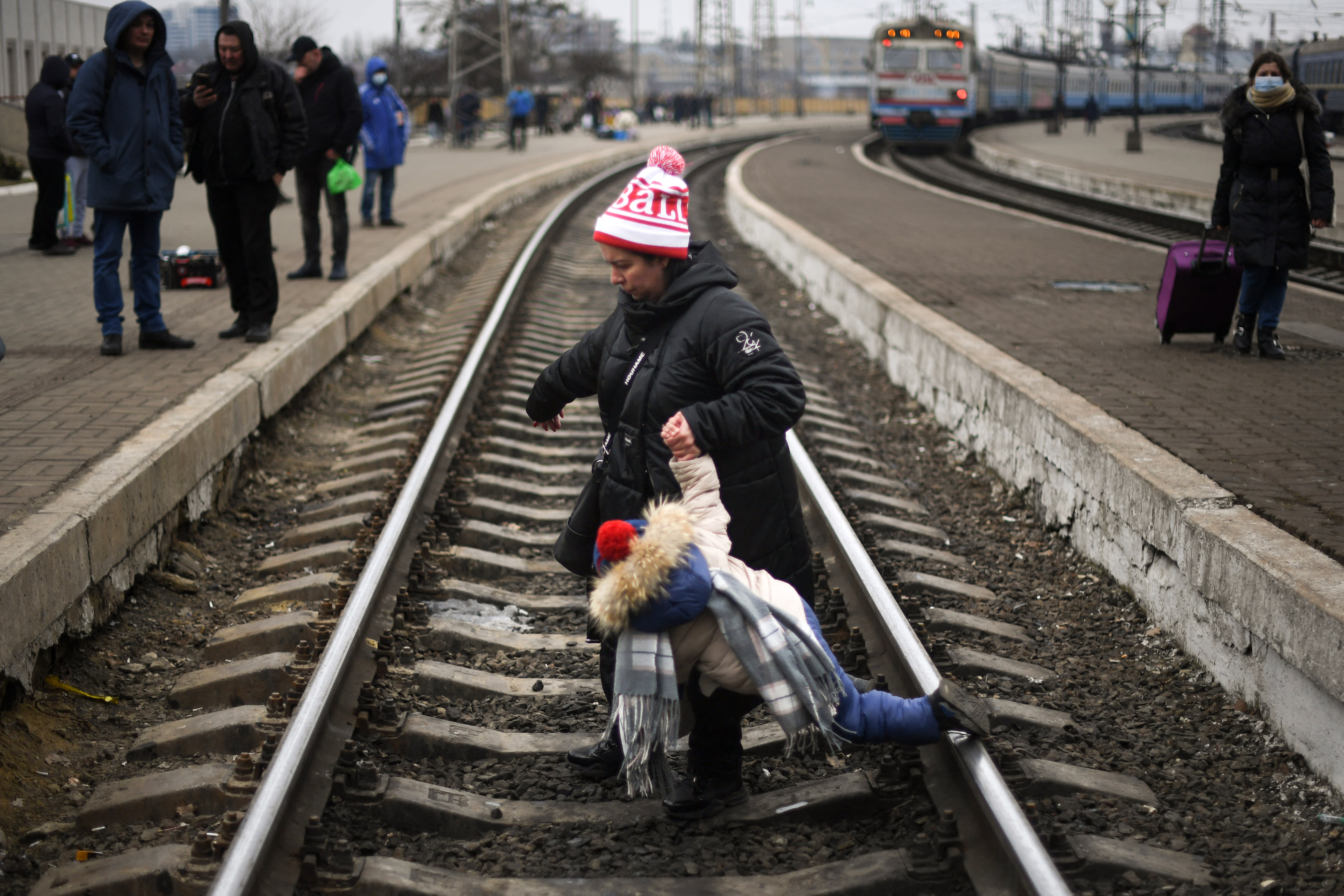 A mother helps a child to cross a railway track at Lviv central train station on March 4, 2022.