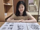 The author is seen here with photocopies of the drawings made by a janitor from her primary school which she has kept. 