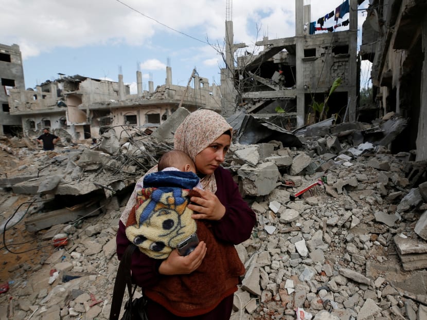 A Palestinian woman carries her child amid the rubble of their houses which were destroyed by Israeli air strikes during the Israel-Hamas fighting in Gaza on Sunday, May 23, 2021.
