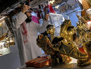A merchant uses a phone to check his styling as he stands before golden boot trophy replicas and other memorabilia at the Souq Waqif market in Doha on Dec 1, 2022, during the Qatar 2022 Fifa World Cup football tournament.
