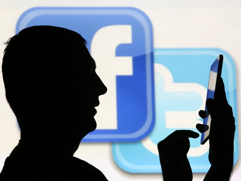 A man is silhouetted as he uses a mini tablet computer while standing in front of a video screen with the Facebook and Twitter logos. Photo illustration: Reuters