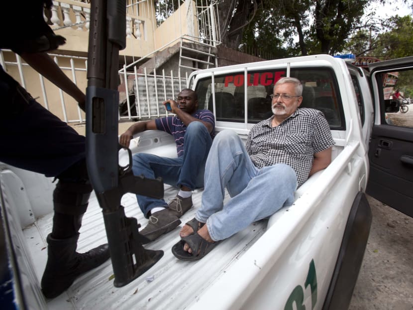 In this Friday, Sept 5, 2014, file photo, Michael Geilenfeld waits in handcuffs as the manager of his orphanage sits with him in the back of a police truck outside the St Joseph's Home For Boys after police closed it down in the Delmas area of Port-au-Prince, Haiti. Photo: AP