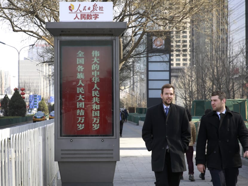Foreigners chat as they walk past a digital display board stating "Long live the great People's Republic of China, Long live the great unity of all ethnic groups" by a China’s state media on display in Beijing. Photo: AP
