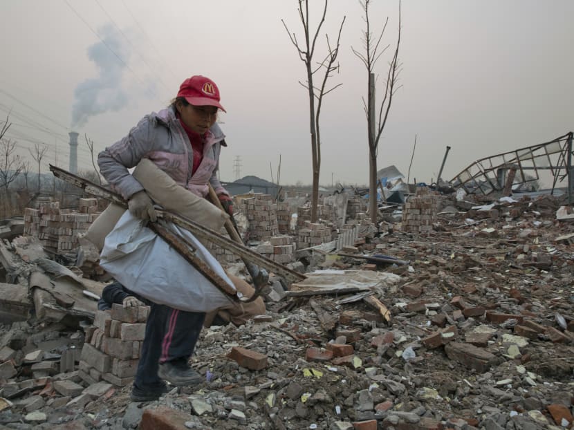 File photo of a scrap collector gathering materials in a demolished neighbourhood near a chimney spewing smoke in Beijing, China on Dec 12, 2015. Photo: AP