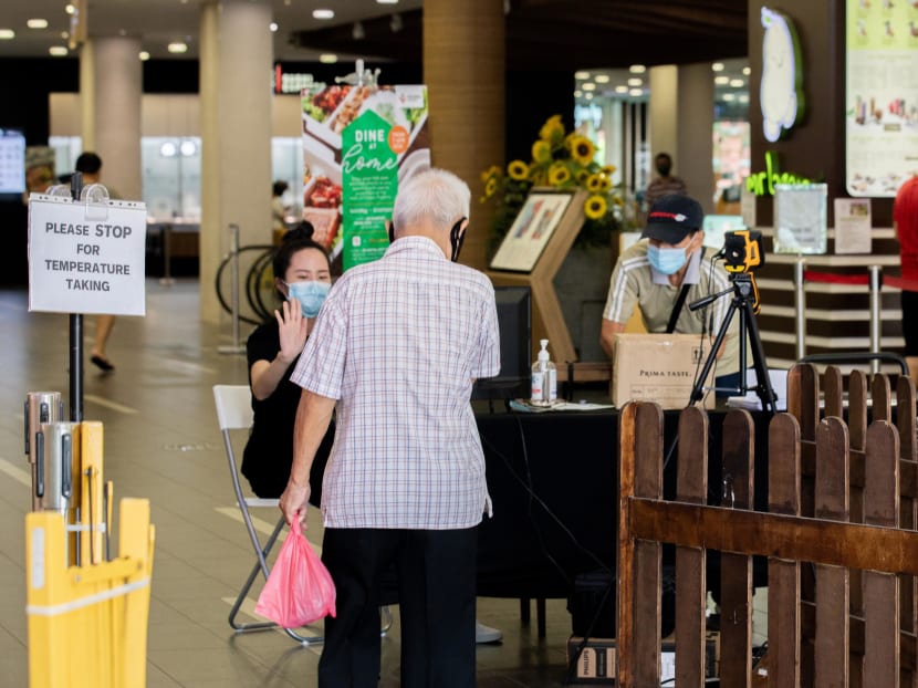 An official is seen checking the temperature of an elderly man before entering YewTee Point Shopping mall on May 10, 2020.