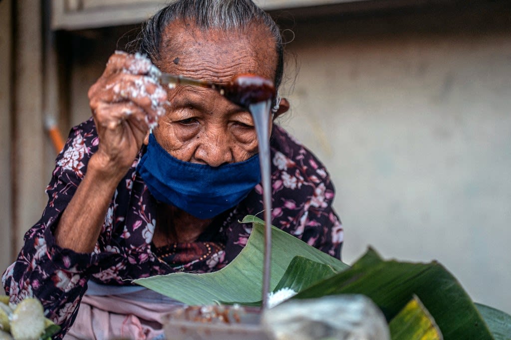 This photo taken on June 22, 2022 shows septuagenarian Mdm Satinem preparing lupis, a traditional sweet dish made from glutinous rice and served with grated coconut and liquid palm sugar, at her street stall in Yogyakarta. This photo taken on June 22, 2022 shows septuagenarian Mdm Satinem preparing lupis, a traditional sweet dish made from glutinous rice and served with grated coconut and liquid palm sugar, at her street stall in Yogyakarta. 