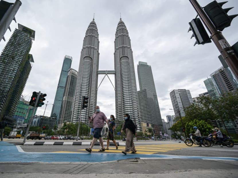 Pedestrians cross a road in front of Malaysia’s landmark Petronas Twin Towers in Kuala Lumpur on Tuesday, Jan 12, 2021, as Malaysian authorities were set to impose tighter restrictions to try to halt the spread of the Covid-19 coronavirus.