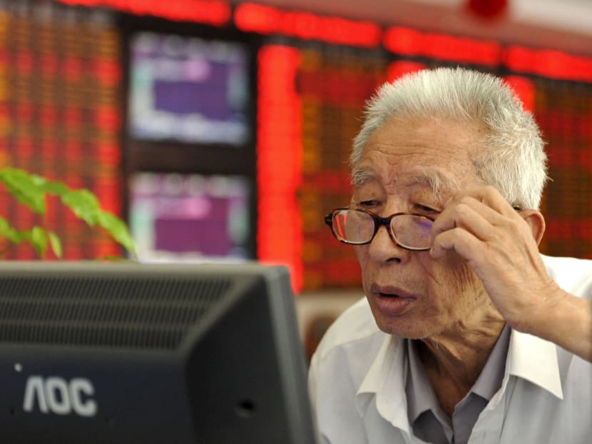 An investor adjusts his glasses as he looks at a computer screen in front of an electronic board showing stock information at a brokerage house in China. The debt implosion and currency collapse that many predict to hit China have failed to materialise. Photo: Reuters