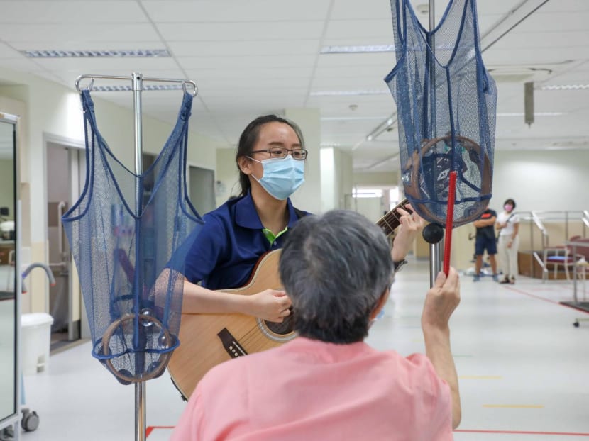 Ms Karen Koh playing the guitar as a patient at St Luke’s Hospital strikes a tambourine during a music therapy session.