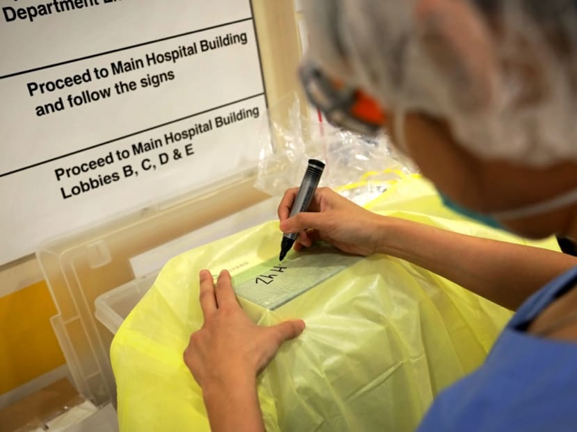An assistant nurse clinician at Tan Tock Seng Hospital who works in both the screening centre and emergency department, writes her name on a gown that she wears as part of personal protective equipment (PPE).