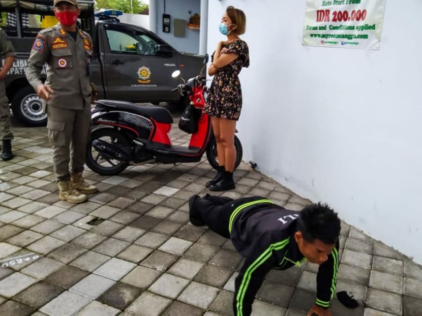 An undated handout picture released on Jan 20, 2021 by Bali's Satpol PP, the provincial public order agency, shows an official looking on while a man performs push-ups as punishment for not wearing or improperly wearing face masks amid the Covid-19 coronavirus pandemic.