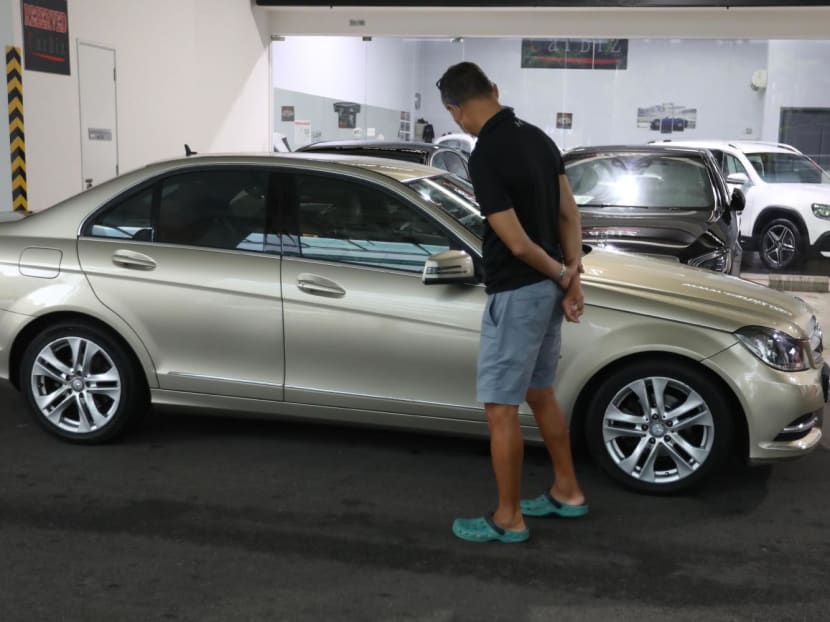 A man looking at a car that was being sold in a showroom in Singapore. A man looking at a car that was being sold in a showroom in Singapore.