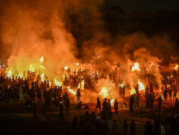 Mourners gather as smoke billows from the abandoned football stadium set ablaze in Malang, East Java on Oct 1, 2023.