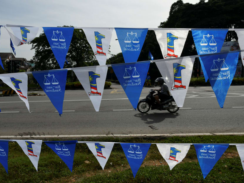 A motorcyclist rides next to flags of the ruling Barisan Nasional coalition in Bangi, Malaysia. The midweek polling date for the Malaysian election has been criticised by both Opposition politicians and Malaysians.