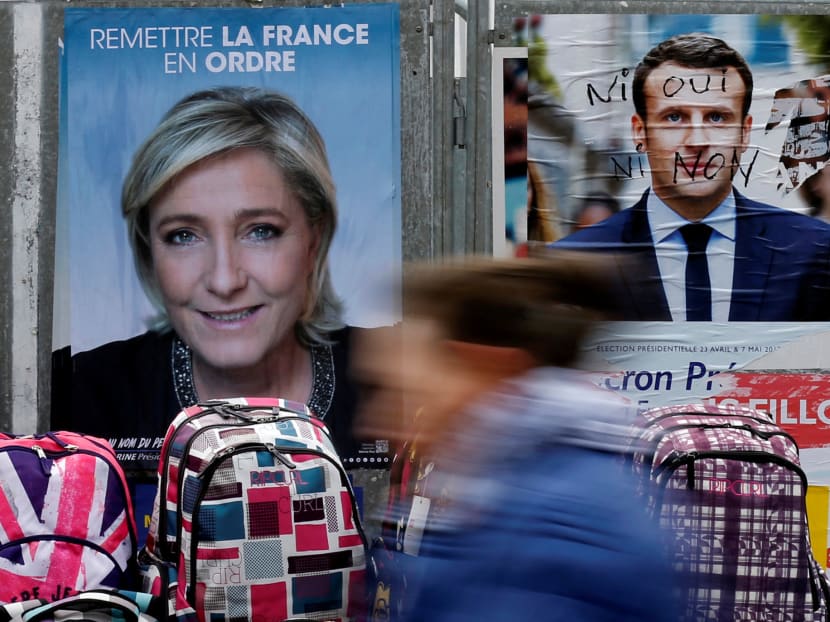 A woman walks past official posters of candidates for the 2017 French presidential election Marine Le Pen, French National Front (FN) political party leader and Emmanuel Macron at a local market in Bethune, France, April 24, 2017.  Photo: Reuters