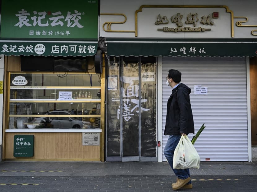 This file photo taken on Nov 19, 2022 shows a man carrying a bag of vegetables walking past closed shops in Beijing’s Chaoyang district due to Covid-19 coronavirus restrictions. 