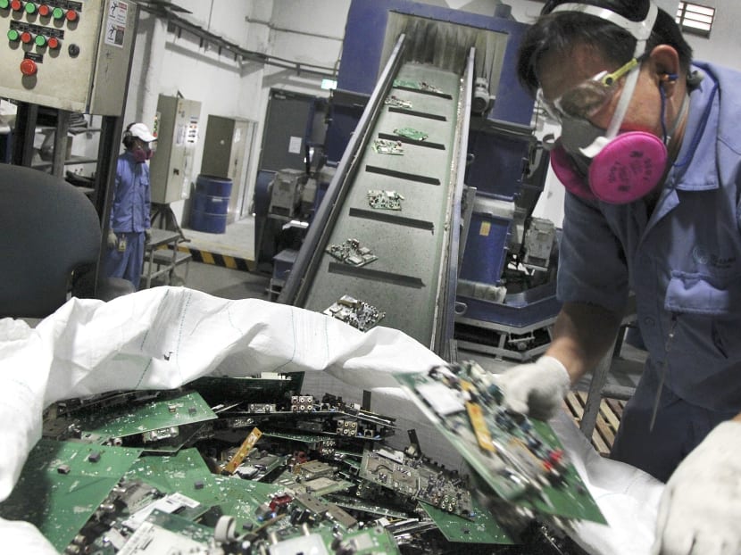 Workers at TES-AMM, a recycling solutions provider, depositing circuit boards removed from electrical appliances onto a conveyor belt before they get crushed into smaller pieces. PHOTO: DON WONG