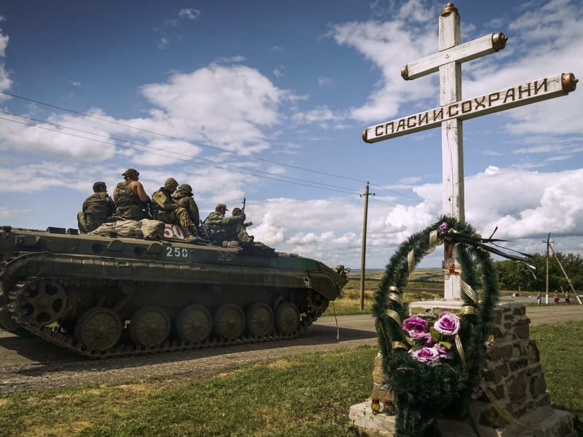 Russia-backed separatist APC rides by an Orthodox cross with a sign reading Save and Guard, with a memorial to the victims of the Malaysian Airlines MH17 plane crash, in the back, near the village of Hrabove, eastern Ukraine, Thursday, July 16, 2015. Photo: AP