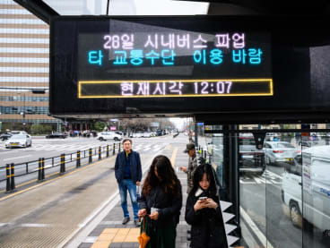 Commuters stand at a bus stop with an electronic display that reads "28th city bus on strike. Please use other transportation" in Seoul on March 28, 2024, as unionised Seoul Bus drivers went on strike, bringing over 7,200 buses to a full stop and disrupting commute hours in the South Korean capital over a wage hike dispute.