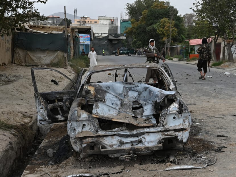 Taliban fighters stand guard near a damaged car after multiple rockets were fired in Kabul on Aug 30, 2021.