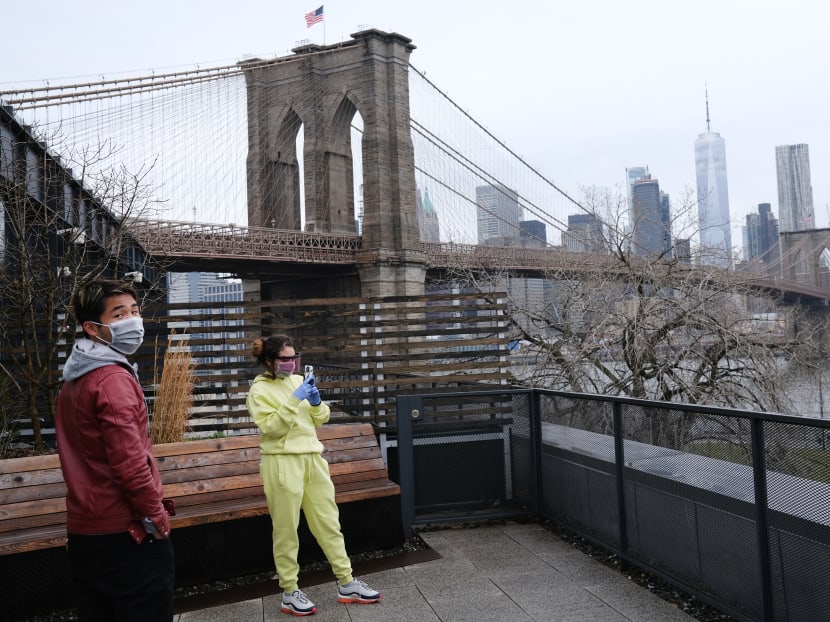 People wearing masks look out from Brooklyn at lower Manhattan on March 28, 2020 in New York City.