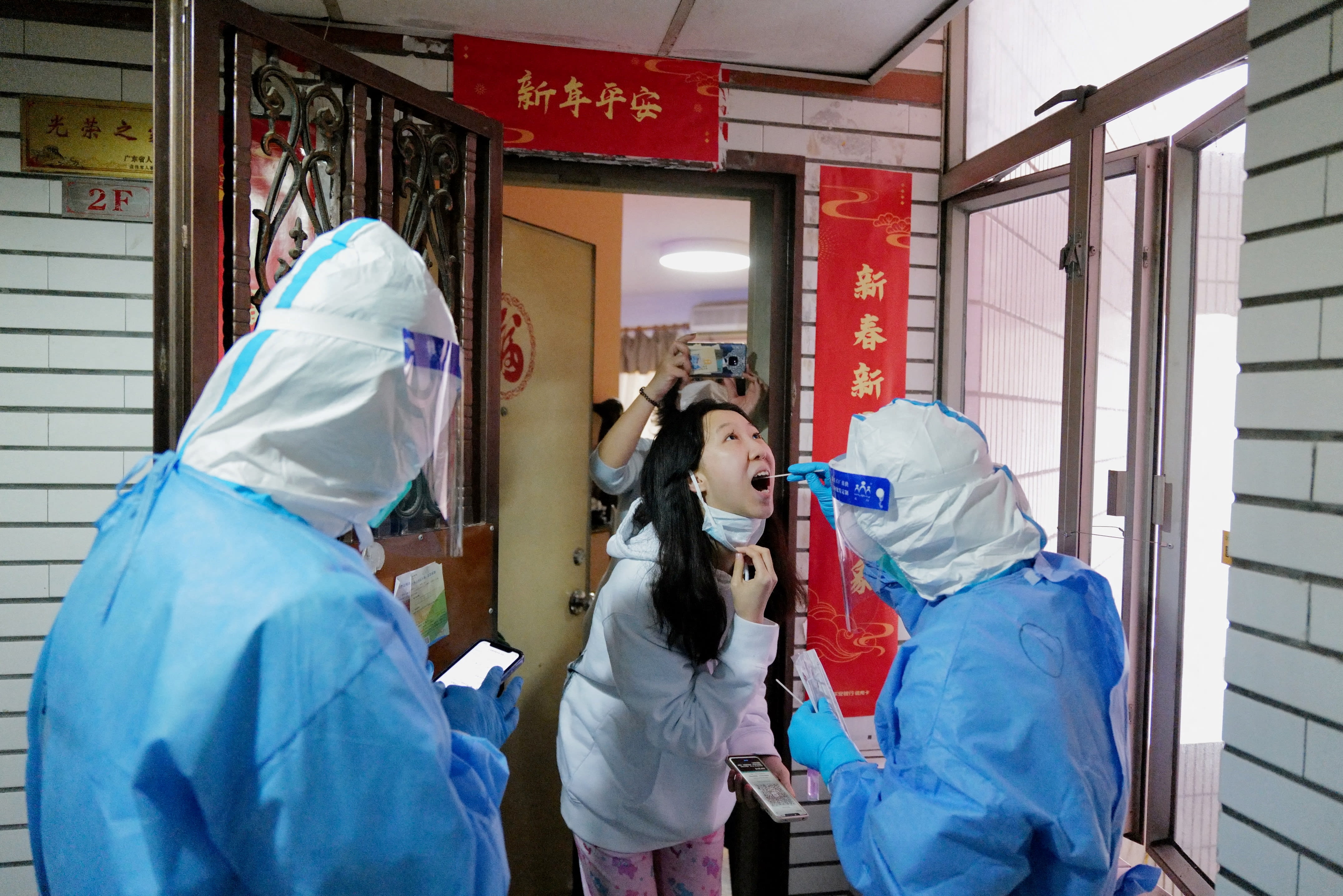 A worker in a protective suit collects a swab from a resident at a residential compound under lockdown, following the Covid-19 outbreak in Shenzhen, Guangdong province, China on March 14, 2022.
