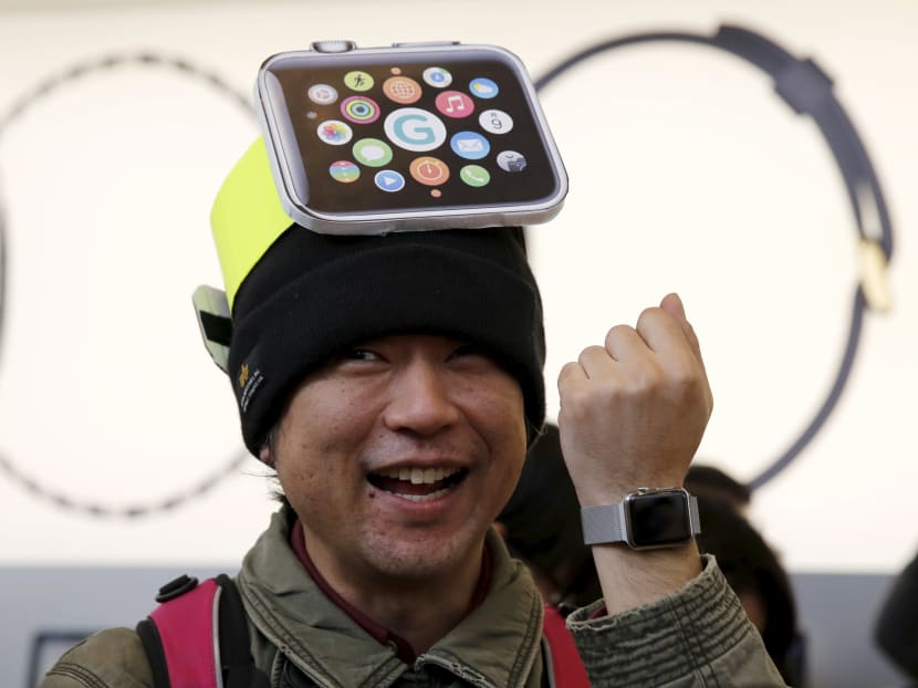 A man wearing cardboard hat depicting an Apple Watch, reacts as he tries on the watch after it went on display the Apple Store at Tokyo's Omotesando shopping district . Reuters file photo