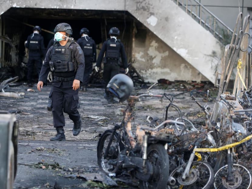 An Indonesian Special Forces Police counter-terrorism squad member walks by burned motorcycles following a blast at the Pentecost Church Central Surabaya in Surabaya in May 2018. It was one of three churches targetted by three Islamic State-linked families of suicide bombers in attacks that killed over 30 people.
