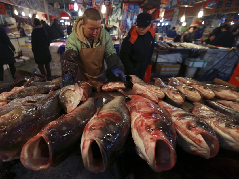 A customer (R) looks on as a vendor arranges fish on display at a stall in a market in China. Photo: Reuters