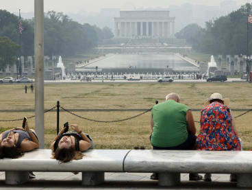 Tourists sit on benches at the base of the Washington Monument as wildfire smoke puts a veil of haze in front of the Lincoln Memorial along the National Mall on June 08, 2023 in Washington, DC.