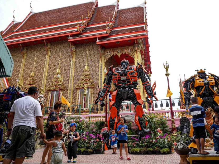This photo taken on June 18, 2017 shows people enjoying giant metal statues inspired by the Transformers franchise, by Ban Hun Lek metalworks, at Wat Tha Kien Buddhist temple in Nonthaburi. As Buddhist temples across Thailand struggle to stay relevant in the modern age, some monks are drawing on a tried-and-true magnet for children: superheroes. Photo: AFP