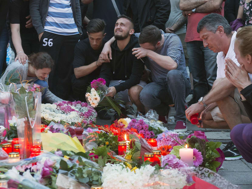 People mourn behind flowers near the Olympia shopping centre where a shooting took place leaving nine people dead the day before in Munich, Germany, on July 23, 2016. Photo: AP