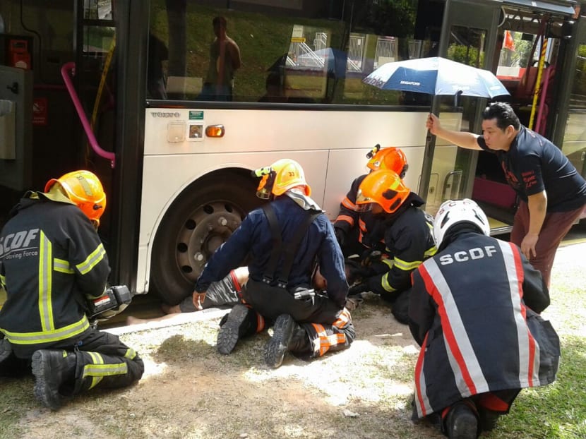 SCDF officers prepare to extricate the man from under the bus, as a passer-by offers some shade. Photo: Bernard Chua