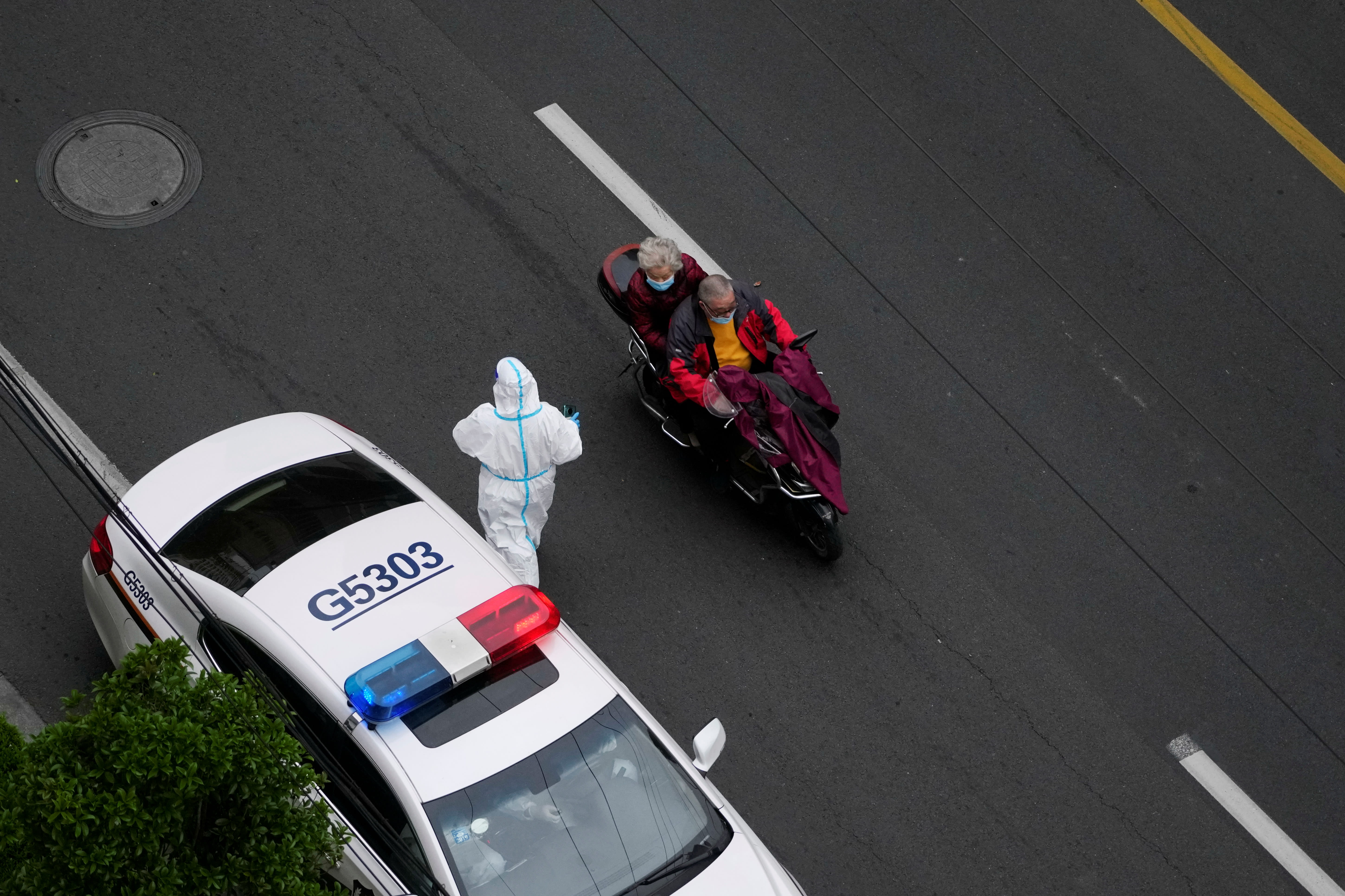 A man rides a vehicle carrying a woman past a police car outside a residential compound, during a lockdown to curb the spread of Covid-19 in Shanghai, China on April 5, 2022. 