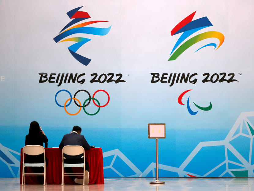 Staff members sit near a board with signs of the 2022 Olympic Winter Games, at the National Aquatics Center in Beijing, China on April 1, 2021.