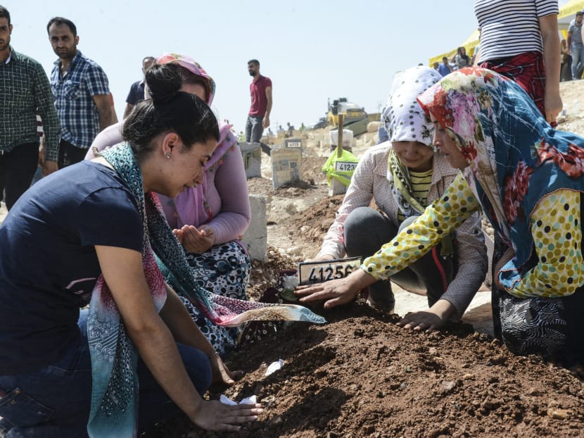 Women gesture as they kneel by a grave at a cemetery during the funeral for the victims of last night's attack on a wedding party that left 54 dead in Gaziantep in southeastern Turkey near the Syrian border on Aug 21.  Photo: AFP