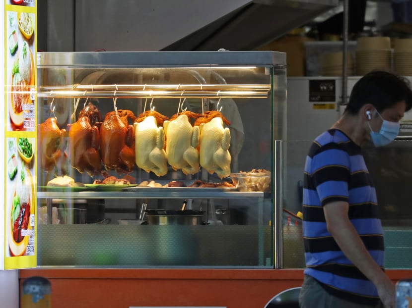 A man walking past a chicken rice stall in Chinatown.