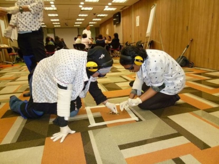 SingHealth staff attempting to pick up coins from the ground with their vision "impaired" to simulate the poor eyesight of some elderly, as part of the Age Sensitisation Workshop designed to help SingHealth better serve its elderly patients. Photo: SingHealth