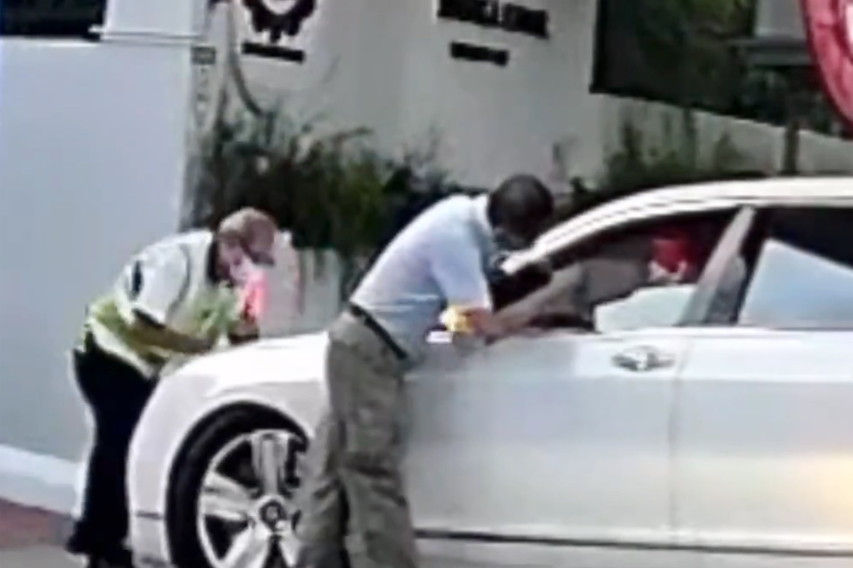 A screenshot from a video showing a security officer and a staff member of Red Swastika School preventing a car from entering the school compound.