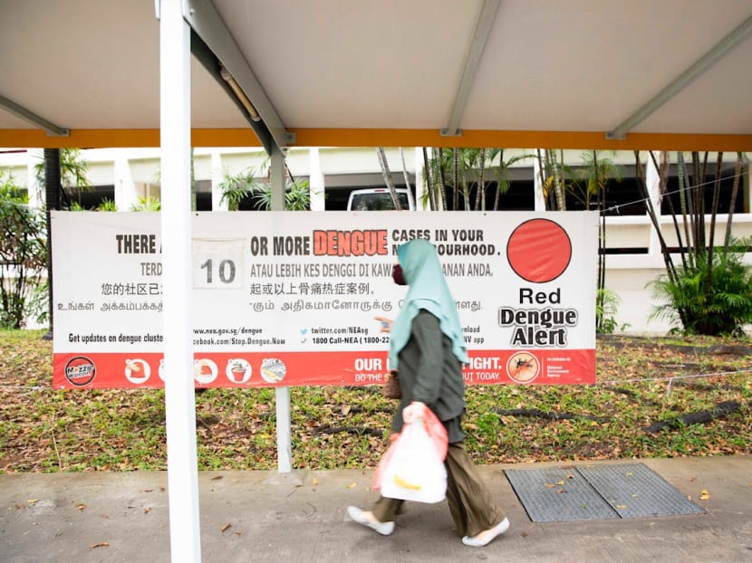 A pedestrian walking along a sheltered pavement with a red dengue alert banner in Woodlands on April 21, 2020.