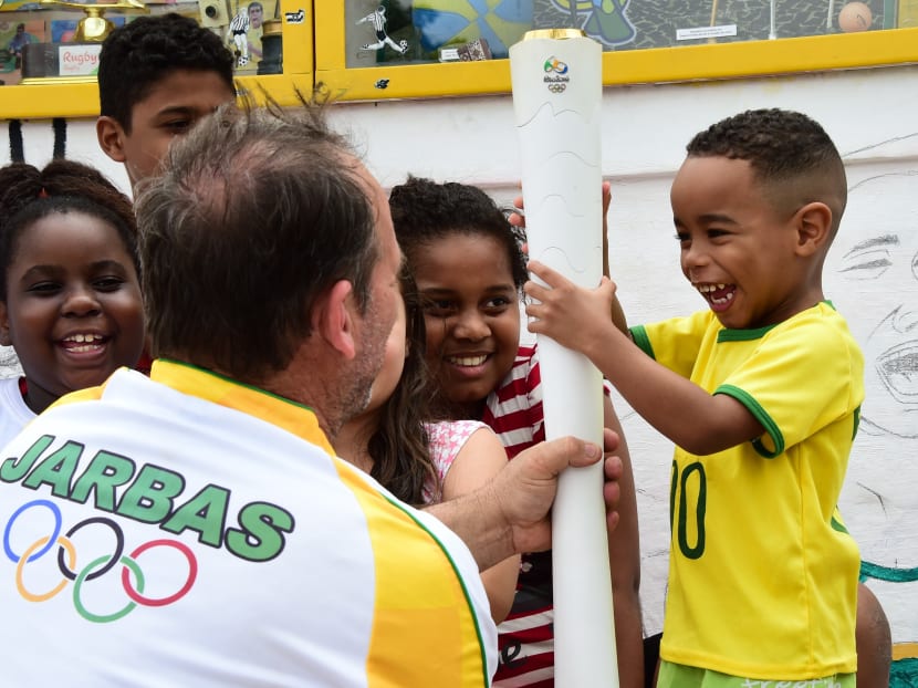 Mr Jarbas Meneghini (back to camera) hands over a replica of the Olympic torch to a young boy. Photo: AFP