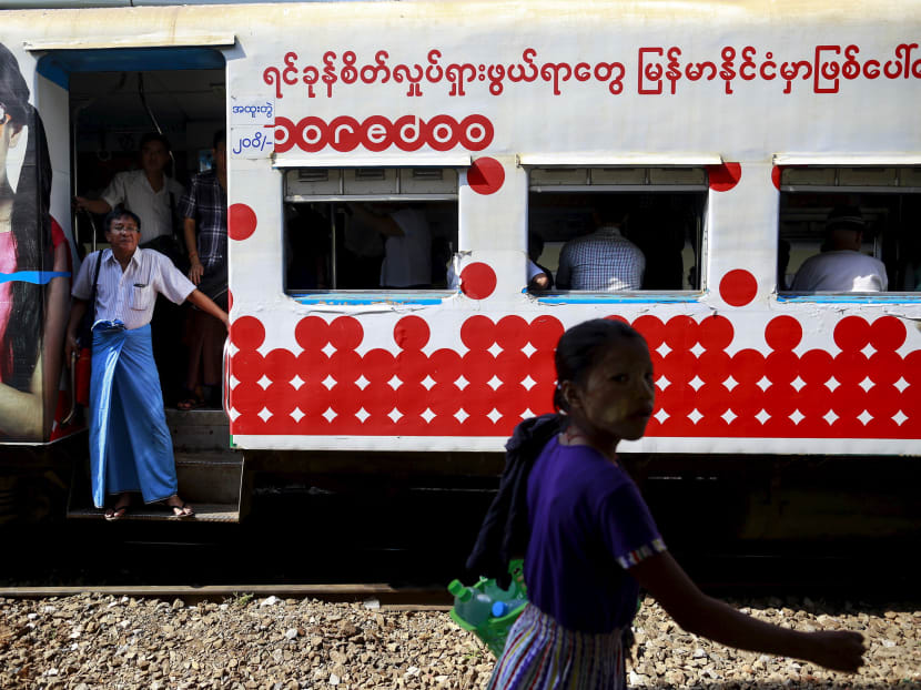 A woman walks pass near a train next people rides a train as they travel in Yangon on May 11, 2015. Photo: Reuters
