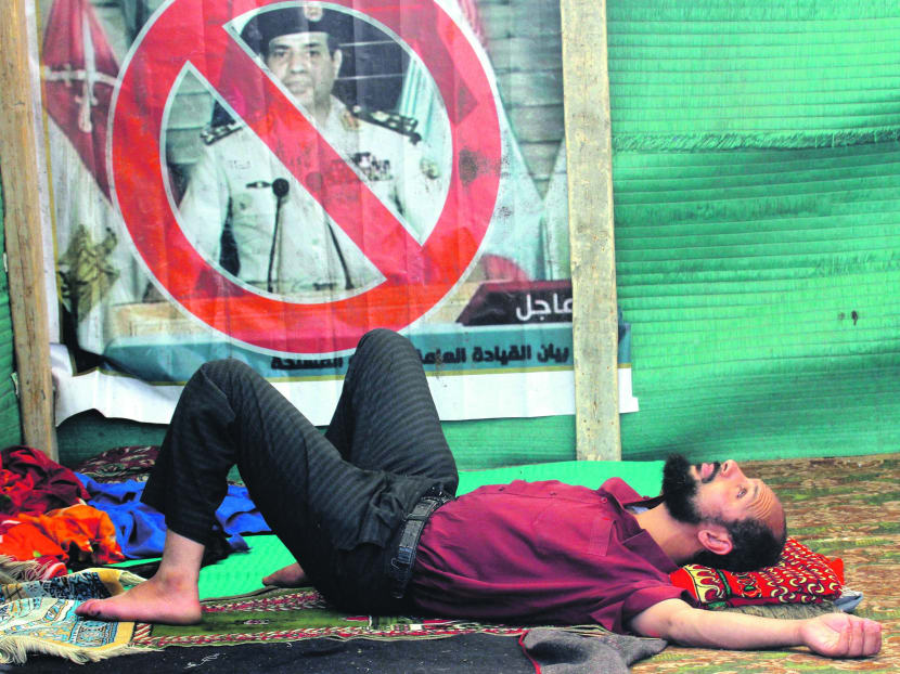 A supporter of Egypt’s ousted President Mohammed Morsi lies on the floor next to a anti-el-Sissi poster in Nahda Square on Aug  12 last year. Photo: AP