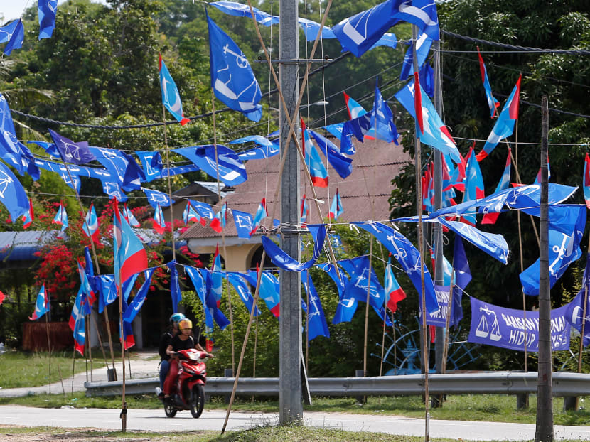 A couple rides a motorcycle past the flags of Malaysia's ruling Barisan Nasional (BN) coalition and opposition Pakatan Harapan pact ahead of the May 9 general election, in Langkawi Island, Malaysia.