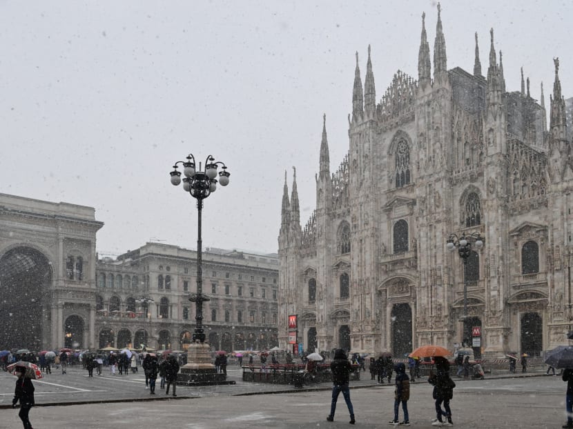 People walking across Piazza del Duomo past the cathedral as snow falls in Milan on Dec 8, 2021.

