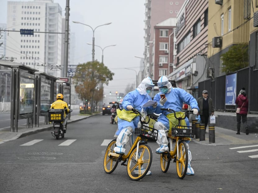 Health workers in personal protective equipments (PPE) carrying Covid-19 coronavirus testing swabs and tubes are seen on bicycles along a street in Beijing on Nov 24, 2022.
