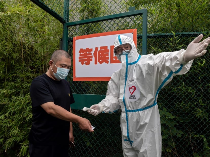 A man wearing a face mask gets his body temperature checked by a health worker as he walks into an outdoor area during a mass testing for Covid-19 at the Xinjiekou urban forest park testing site in Beijing on June 24, 2020.